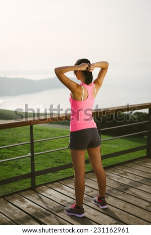 Female athlete getting ready for sport and fitness exercising. Rear view of full body sporty woman looking the sea.