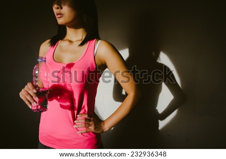 Female athlete taking a fitness workout rest for drinking water. Young woman on a circle of light projecting shadow in a wall.