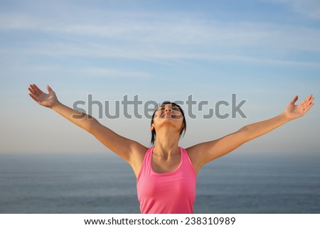 Happy woman enjoying relaxing breeze and freedom by the sea. Joyful asian girl raising arms to the sky.