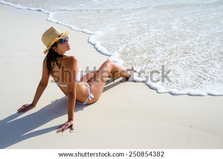 Relaxed woman tanning at beach seashore. Beautiful brunette in white bikini enjoying summer vacation relax.