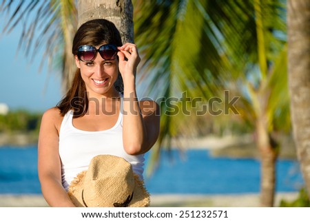 Happy woman on tropical vacation smiling. Brunette girl enjoying caribbean travel and raising sunglasses for looking at camera.