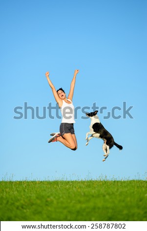 Joyful sporty woman and dog jumping and having fun after running and exercising outdoor together. Female athlete and her pet celebrating sport success and freedom.