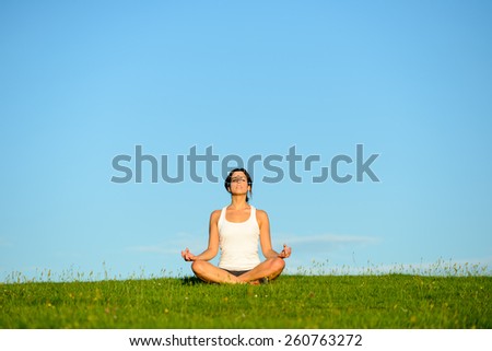 Young woman doing yoga relaxing and breathing exercise outdoor. Relax and tranquility at green grass field towards blue clear sky.