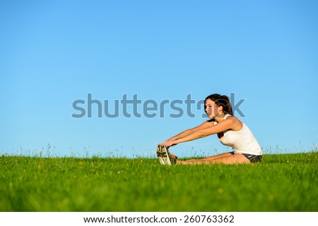 Sporty woman doing fitness stretching legs exercise. Brunette athlete on outdoor workout.