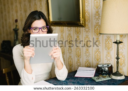 Woman at vintage looking home working and reading on digital tablet. Female young worker or photographer doing her job in retro desk with old camera.