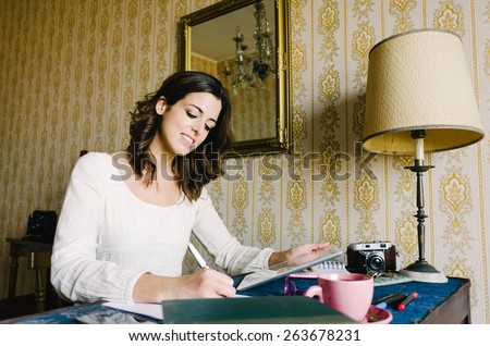 Woman working at home. Female entrepreneur writing and holding digital tablet. Female young worker or student doing her job in retro desk. Vintage filtered image.