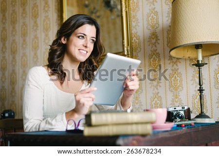 Woman at vintage looking home working and reading on digital tablet. Female young worker or student doing her job in retro desk. Vintage filtered image.