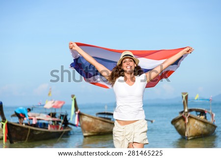Happy woman having fun at Krabi beach with Thailand flag. Beautiful brunette enjoying travel to Asia.