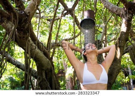 Relaxed happy woman taking spa shower outdoor in exotic garden.