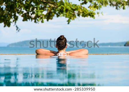 Relax and spa concept. Woman with a flower in hair relaxing in a pool towards the sea \
at Krabi, Thailand.