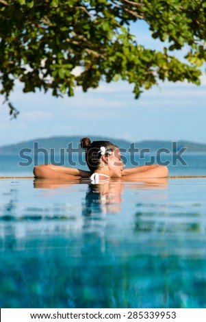 Relax and spa concept. Woman with a flower in hair relaxing in a pool towards the sea at Krabi, Thailand.