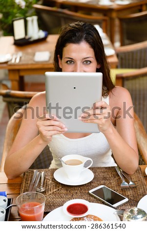 Happy woman on summer vacation having breakfast and reading on digital tablet in tropical resort outdoor cafe.