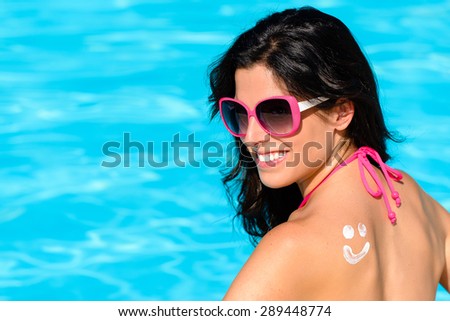 Happy woman with sunscreen lotion funny smiley on her back enjoying summer vacation at swimming pool. Beautiful brunette sunbathing. Skin care and sun protection concept.