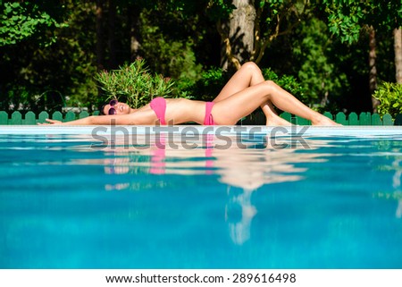 Joyful beautiful woman in bikini sunbathing at poolside on summer vacation. Relax and joy on summertime.