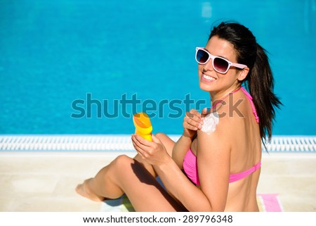 Woman applying sunscreen or suntan lotion in her shoulder for solar skin protection at swimming pool. Brunette girl enjoying summer vacation.