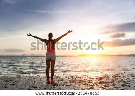 Sporty woman enjoying relax and freedom towards the sun and sea on sunset at the beach. Tranquility and bliss concept.