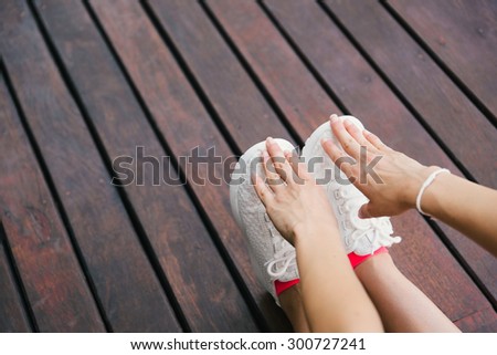 Fitness lifestyle and sport concept. Sporty footwear and female hands close up. Woman stretching legs outdoor on wooden floor.