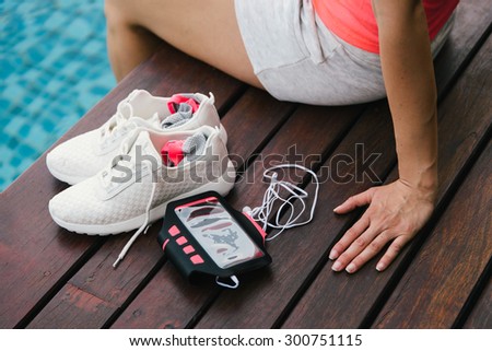 Fitness and healthy lifestyle concept with sporty white footwear and armband for smartphone. Woman with feet into water at poolside.