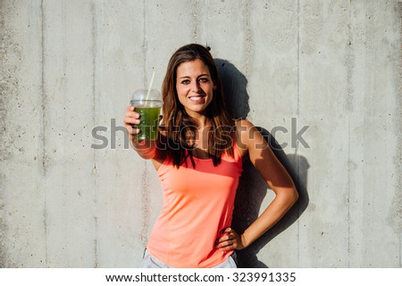 Sporty woman offering detox green smoothie. Happy sportswoman showing healthy fruit and vegetables drink. Fitness lifestyle and nutrition concept.