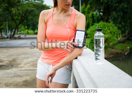 Fitness woman pressing smartphone button on armband for starting mp3 or running workout app. Female athlete getting ready for outdoor training at city park.