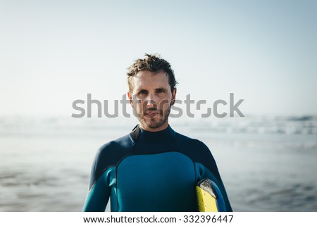 Male surfer beach lifestyle portrait. Man in wetsuit with bodyboard surfing equipment.