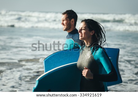 Young couple of bodyboard surfers running. Surfing and outdoor sport lifestyle concept. Woman and man after bodyboarding.