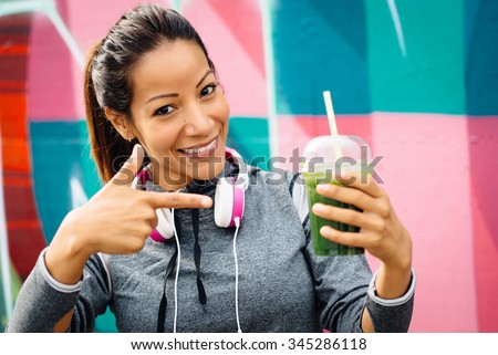 Successful fitness urban woman taking a rest for drinking and recommending detox smoothie. Healthy nutrition and lifestyle concept.