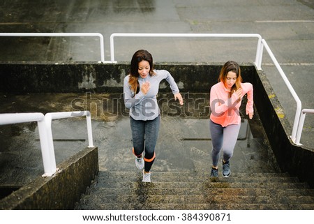 Urban fitness women running and climbing stairs for legs power and strength training. Female athletes working out outdoor in rainy winter day.