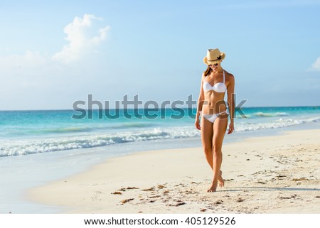 Relaxed woman in bikini enjoying tropical beach and caribbean summer vacation. Fit tanned brunette enjoying a walk by the sea at Playa Paraiso, Riviera Maya, Mexico.