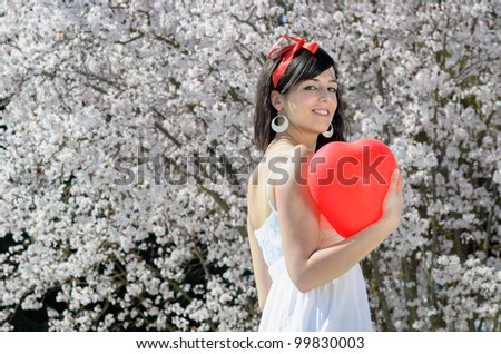 Spring love hearth balloon. Girl holding read hearth shape balloon on spring flowers tree background.