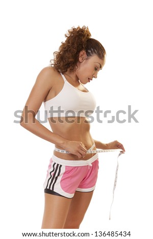 Woman with six pack looks down at a measuring tape around her waist, isolated on white background.