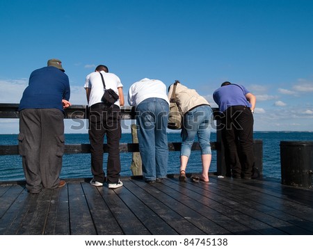 Group of curious young people standing on a wooden deck and looking at the sea ocean