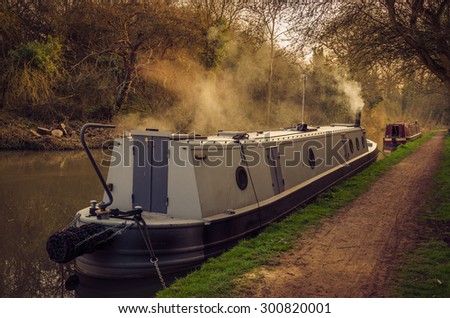 Grand Union Canal of England - Grey narrow boat, seen from its stern, moored on a stretch of the Grand Union Canal by the town of Leamington Spa, Warwickshire, English West Midlands.