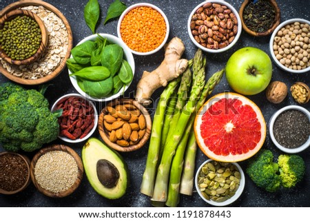 Superfoods on black stone background. Legumes, nuts, chia, avocado, grapefruit, beans, goji, green apple and asparagus and quinoa. Top view.