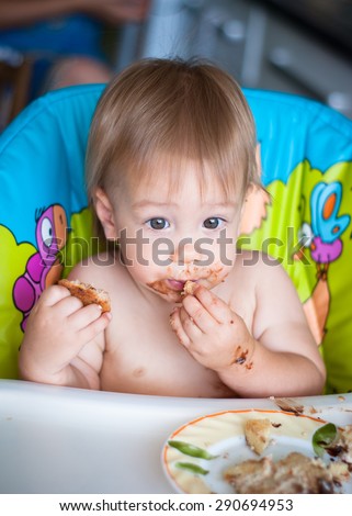 Child eats cake in the highchair. His face and hands smeared with cake
