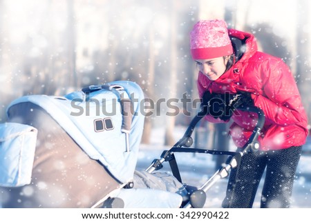 A young mother looks at the baby in a stroller for a walk in the park in winter