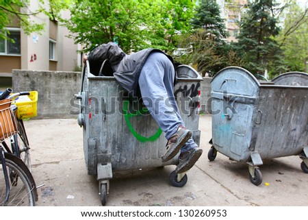 A homeless man looking for food in a garbage dumpster. / Urban Poverty