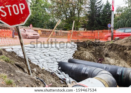 White sandbag bags are full with sand in wall formation to hold the Earth near traffic road. Industrially isolated pipes for distance heating passes under the road.