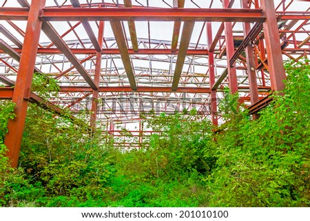 Old rusty abandoned industrial structure with beams and vegetation growing on it with a melancholic look suggesting long lasting work.