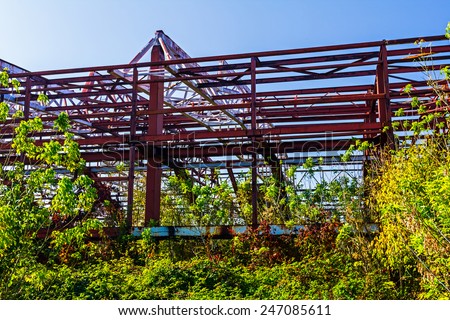 Old rusty abandoned industrial structure with beams and vegetation growing on it with a melancholic look suggesting long lasting work.