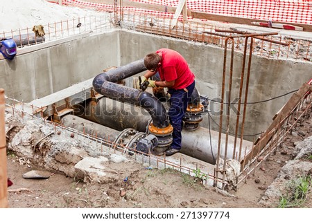 Metal worker is grinding weld on pipe junction completing a manhole for heating pipeline system.
