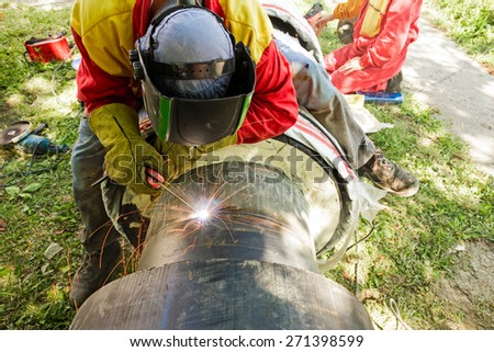 Welder working on a pipeline in construction site wearing overall and safety equipment