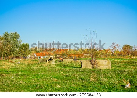 Concrete pipes scattered on green meadow with city nearby.