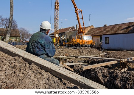 Construction worker is resting on pile of earth, in a busy construction site.