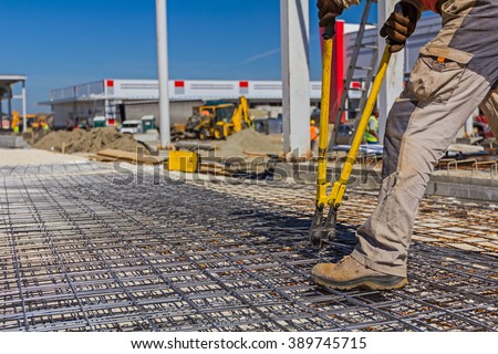 Worker is cutting reinforcement mesh with bolt cutters at building site.