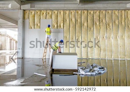 Workers are assembly gypsum wall. Plasterboard is under construction using wooden ladder.
