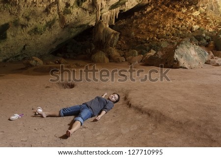 Alone woman sleeping on ground in tropical cave, Thailand