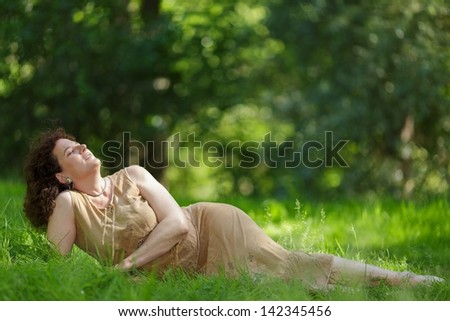 Middle aged mature woman lying in fresh spring grass under sunlight