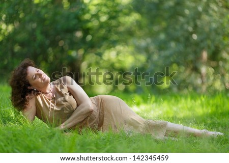Middle aged mature woman lying in fresh spring grass under sunlight