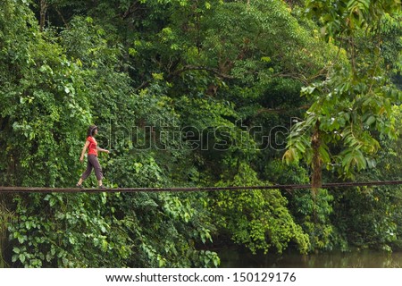 Woman walking on wooden suspended bridge in jungle, Thailand